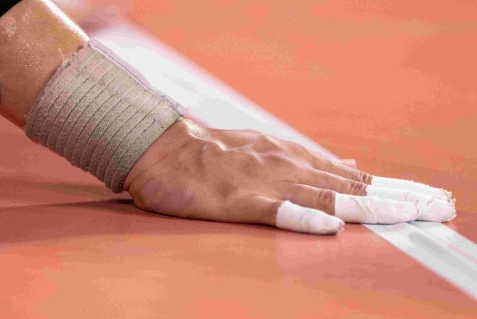 a hand with tape on the fingers touches the white line on a court 
