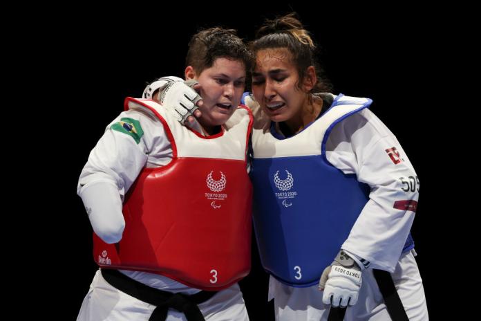 Two female taekwondo fighters embrace after a competition bout. 