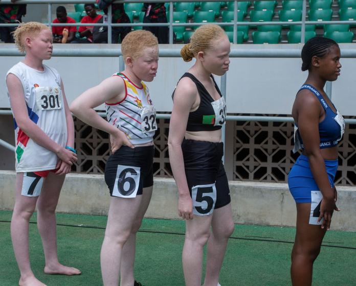 Four female runners stand in line with numbers attached to their uniforms as they wait to be called up to race.