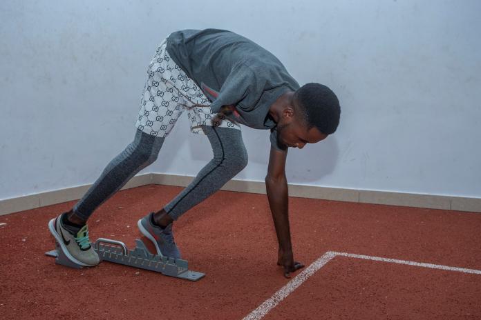 A male athlete without a right arm below the shoulder stands in the starting blocks on an indoor track.