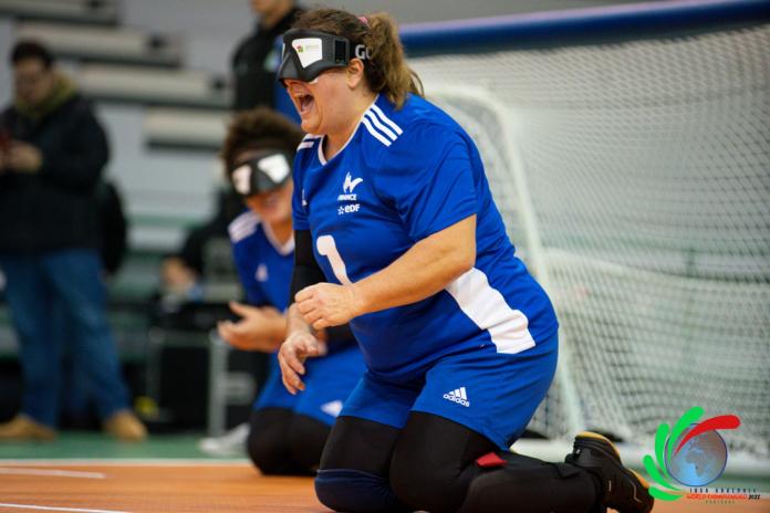 A female goalball player is sitting in front of the goal