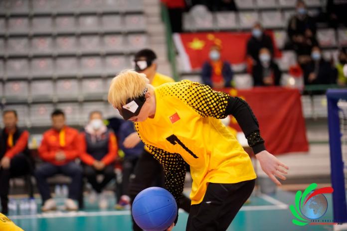 A male goalball player rolls the blue goalball in front of his net.