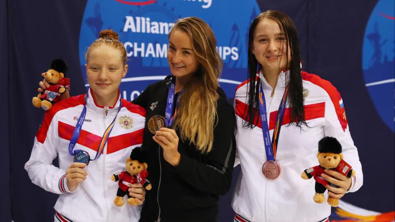 three female Para swimmers on the podium holding up their medals