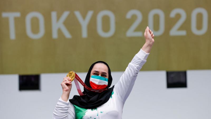 A woman celebrating with her gold medal in front a Tokyo 2020 banner