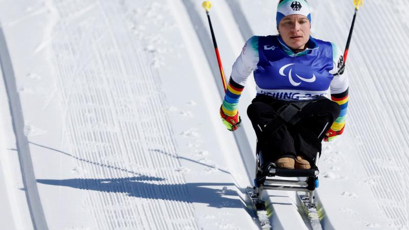 A female sit-skiing athlete is racing down hill in the cross-country segment of a Para biathlon event