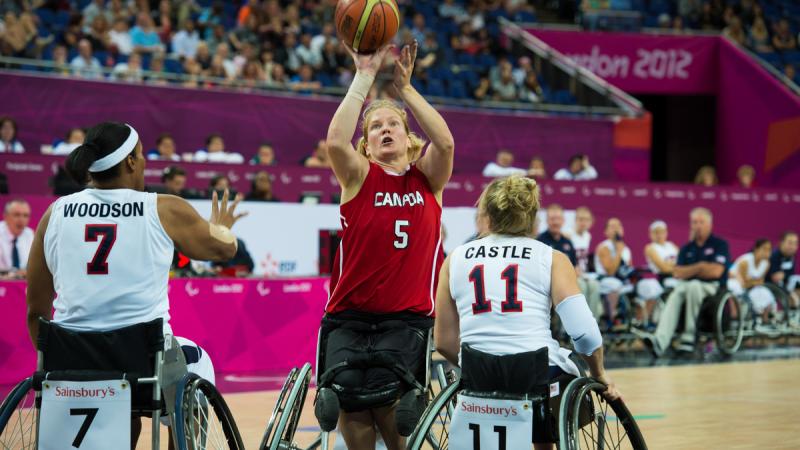 A picture of a woman in a wheelchair shooting between two defenders during a wheelchair basketball match.