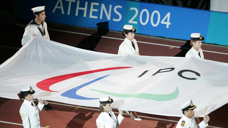 Six people carry a flag with the Paralympic symbol into a stadium