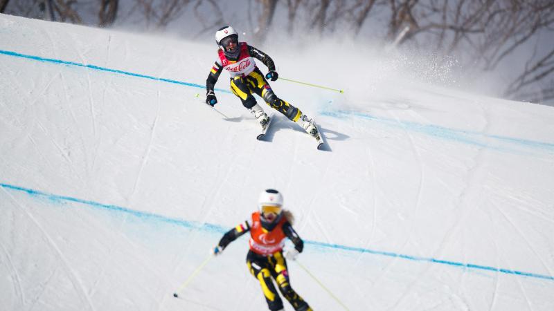 a female vision impaired skier and her guide head down the slope