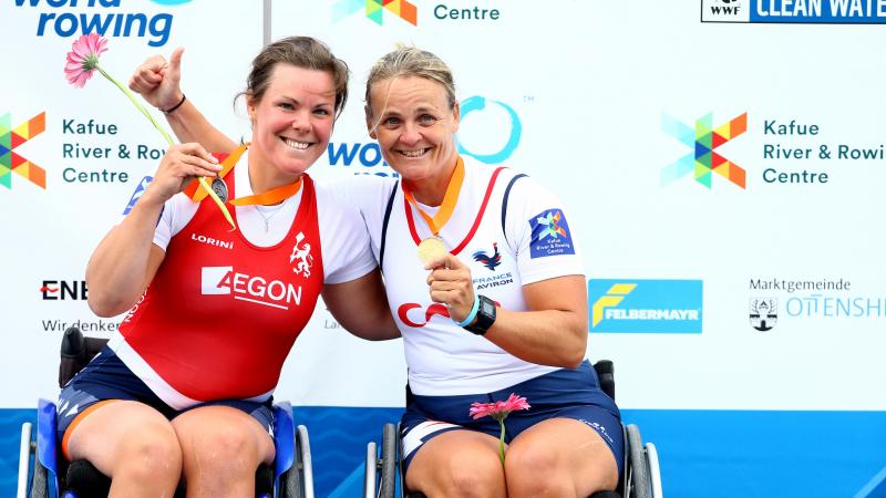 two female Para rowers in wheelchairs hug on the podium
