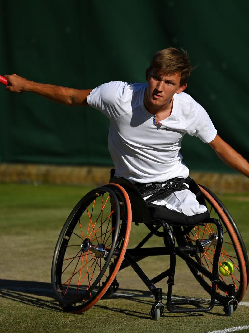 A male wheelchair tennis player extends his arms after returning the ball.