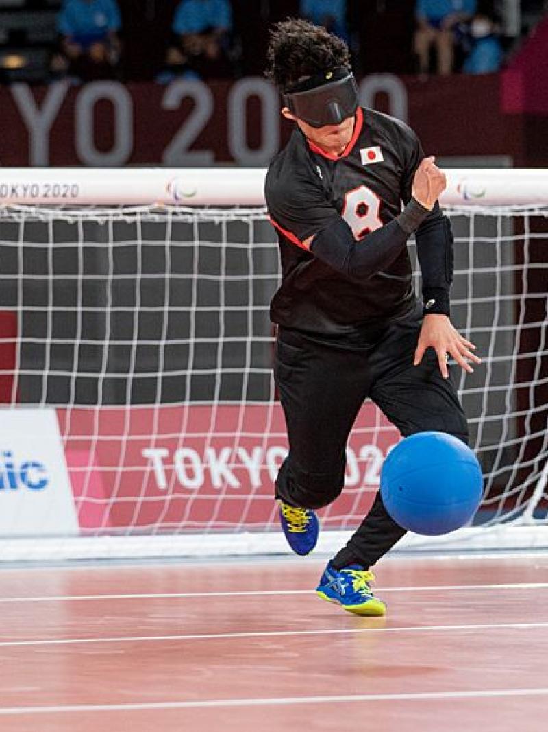 A male goalball player rolls the blue goalball in front of his net.