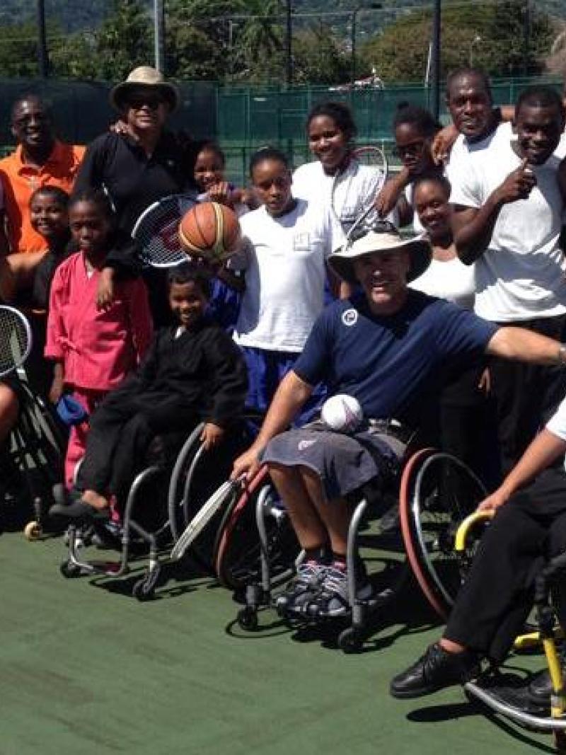 Group picture of people in wheelchairs and standing on a tennis court