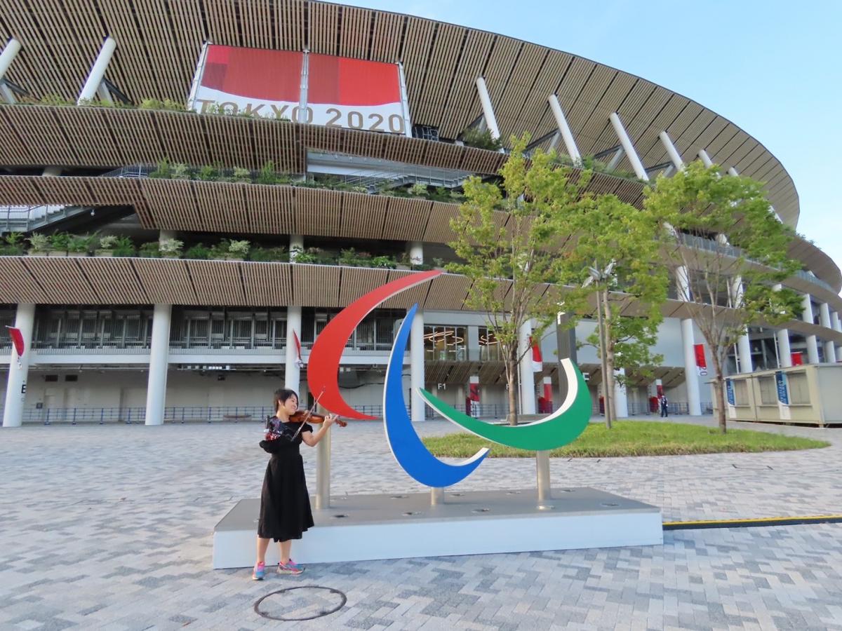 A former Paralympian poses with a violin in front of the Agitos symbol at the Olympic Stadium in Tokyo.