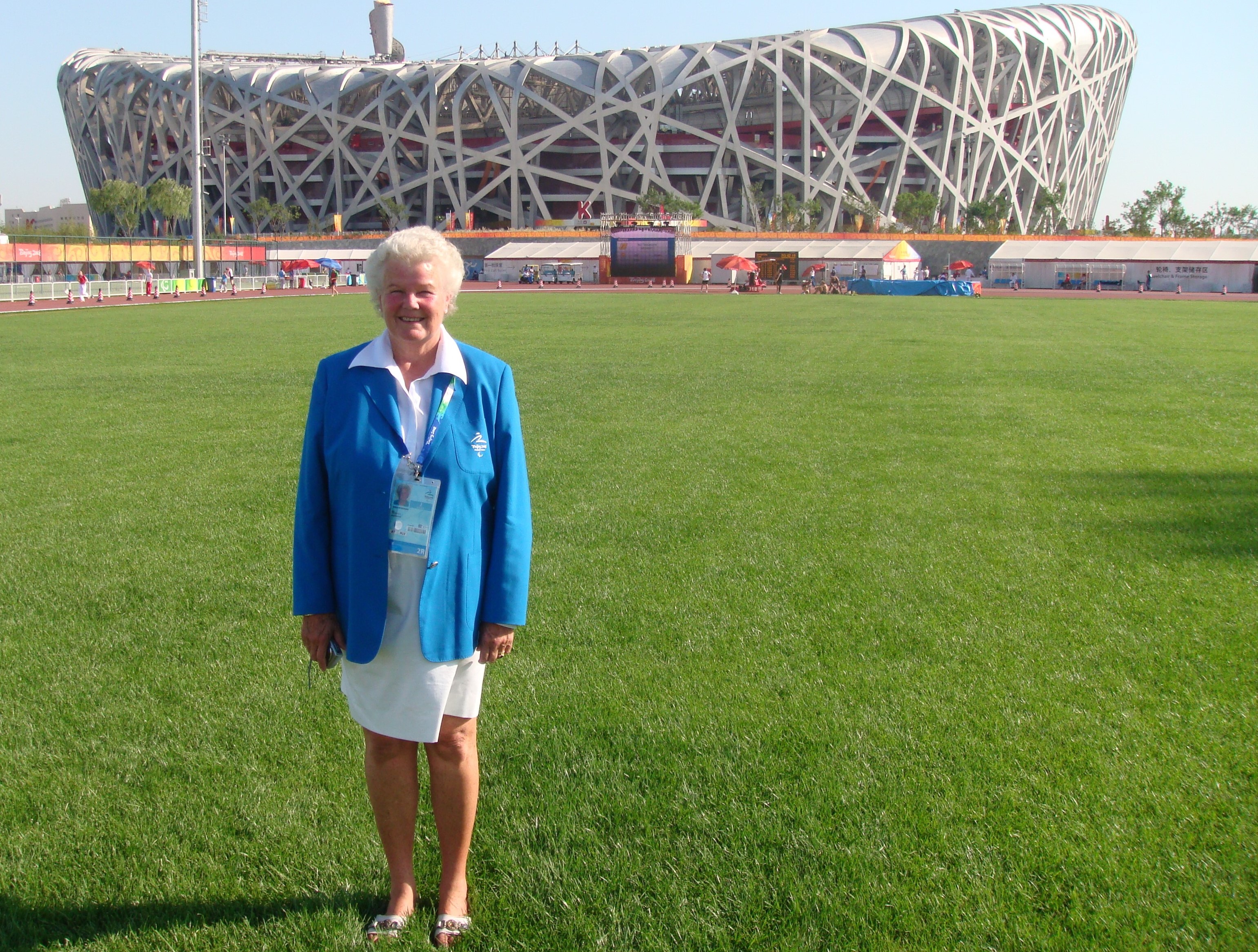 A woman in white skirt and blue jacket posing in front of the athletics stadium during the Beijing 2008 Paralympics