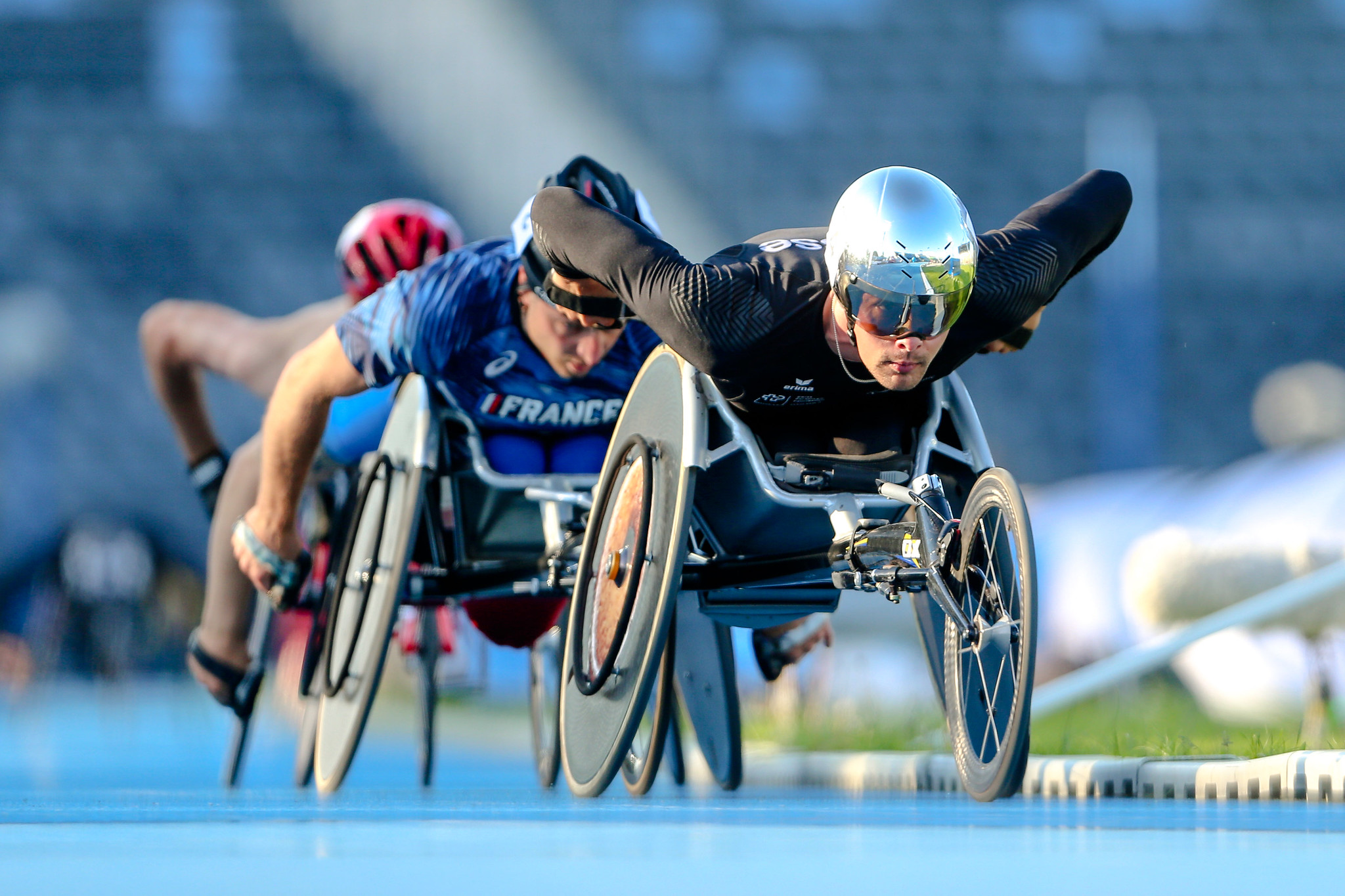 A men in a racing wheelchair leading a competition being followed by two competitors