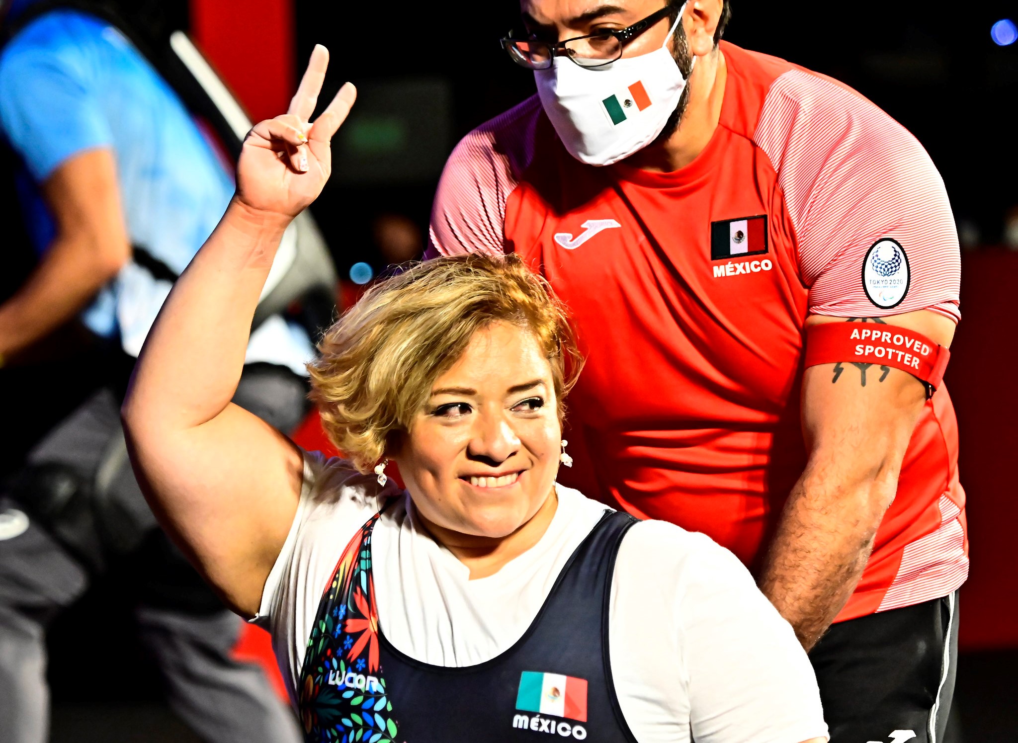 A woman smiling and raising her arm in a wheelchair chair being pushed by a man