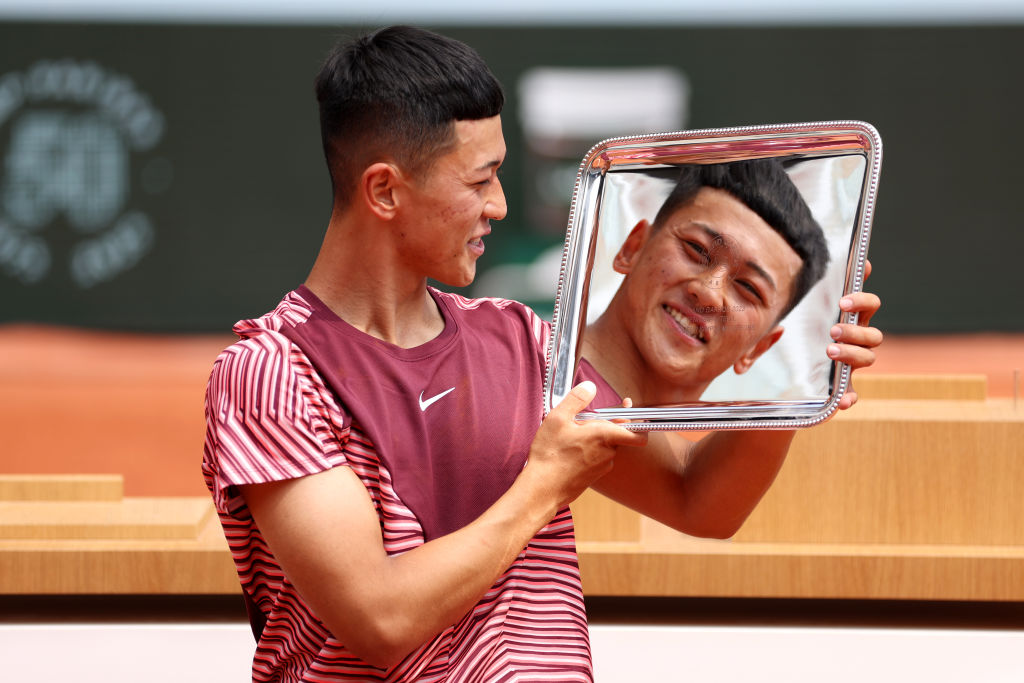 A male athlete holds the French Open trophy. His face is reflected on the silver trophy. 