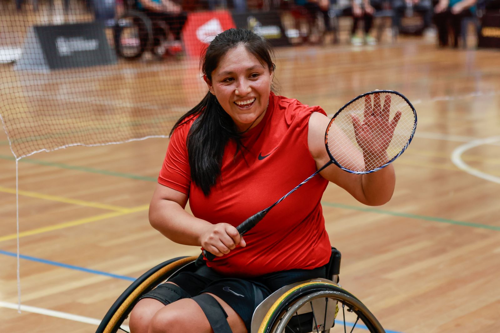 A female Para badminton player, who competes in a wheelchair, holds a racquet and smiles