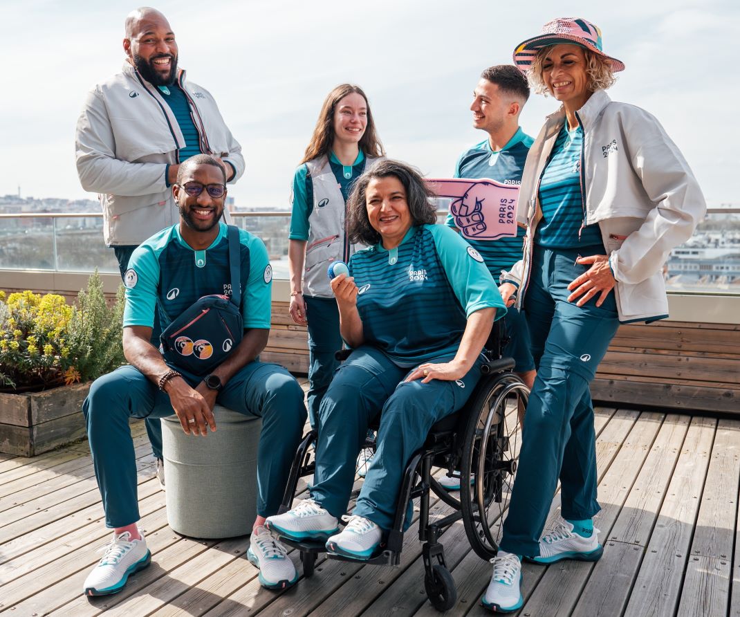 Six male and female volunteers pose for a photograph wearing the Paris 2024 volunteer uniform.