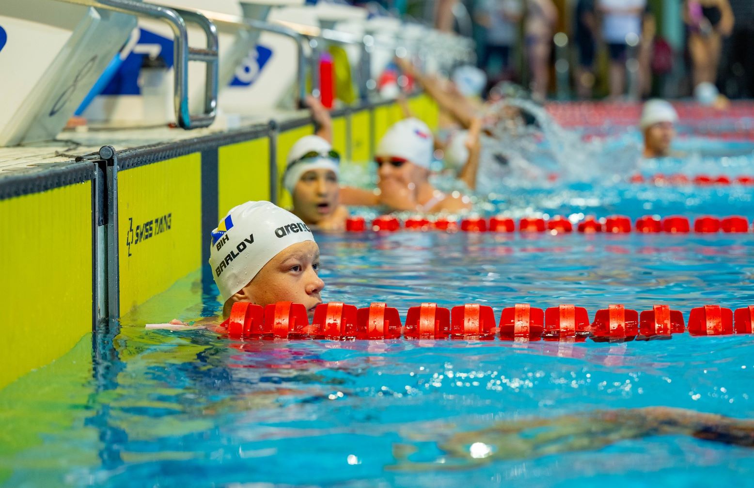 A male swimmer in a swimming pool lane with other swimmers in the background