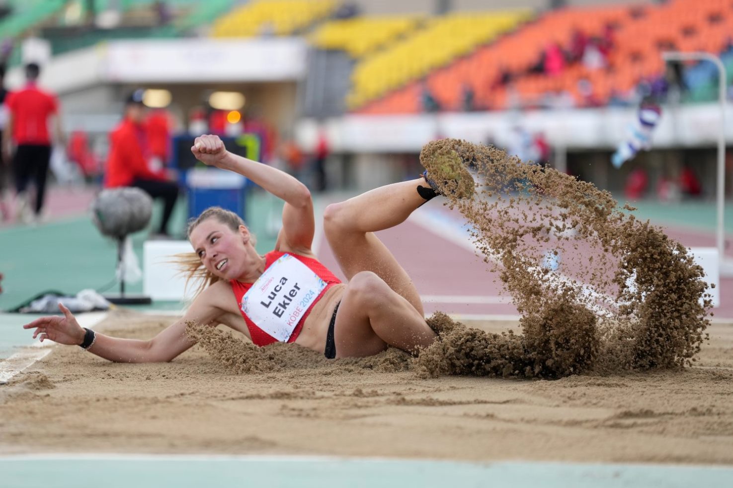 A female athlete landing in the sand in a long jump event