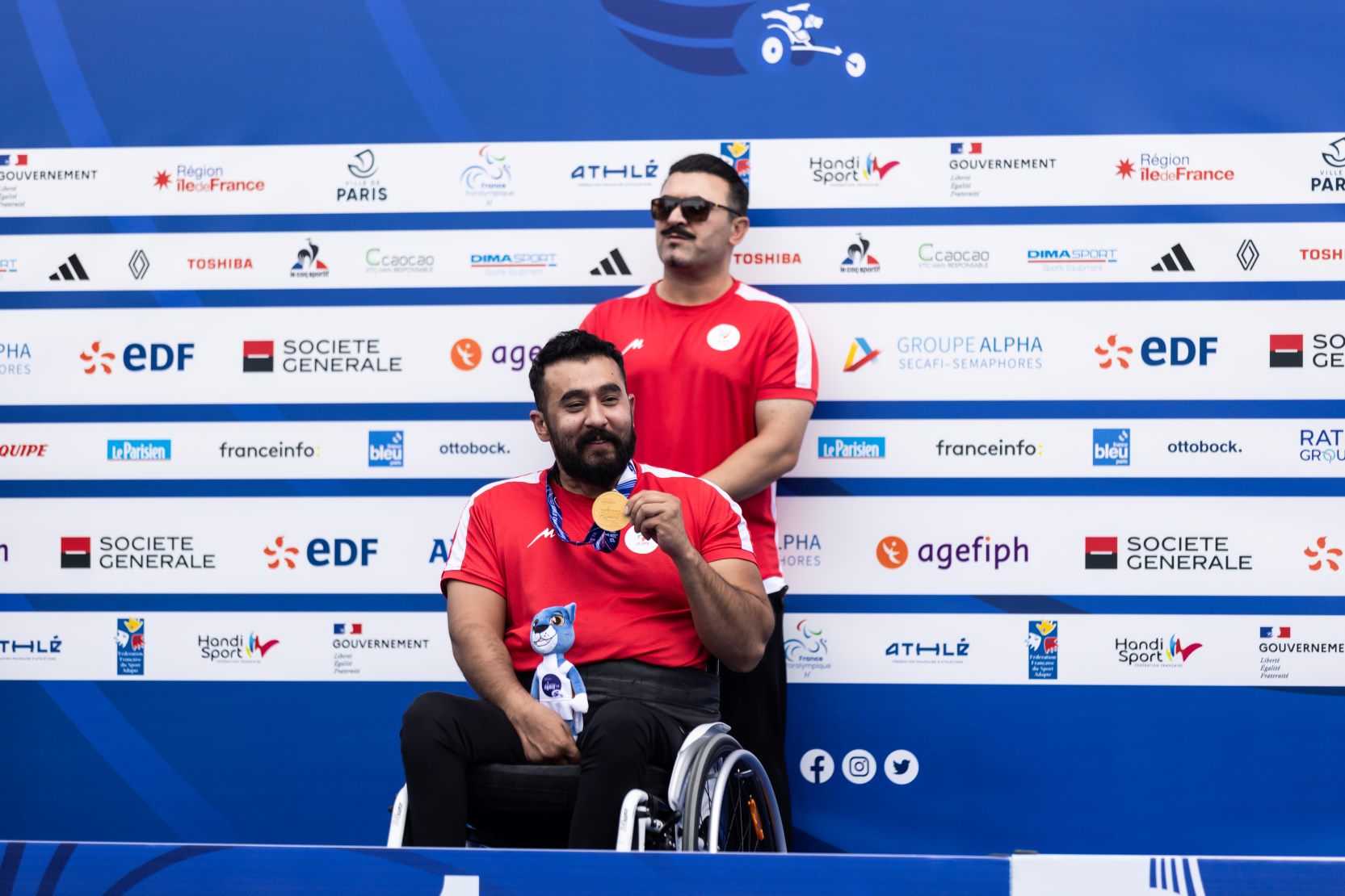 A man in a wheelchair showing a medal with a man standing behind him