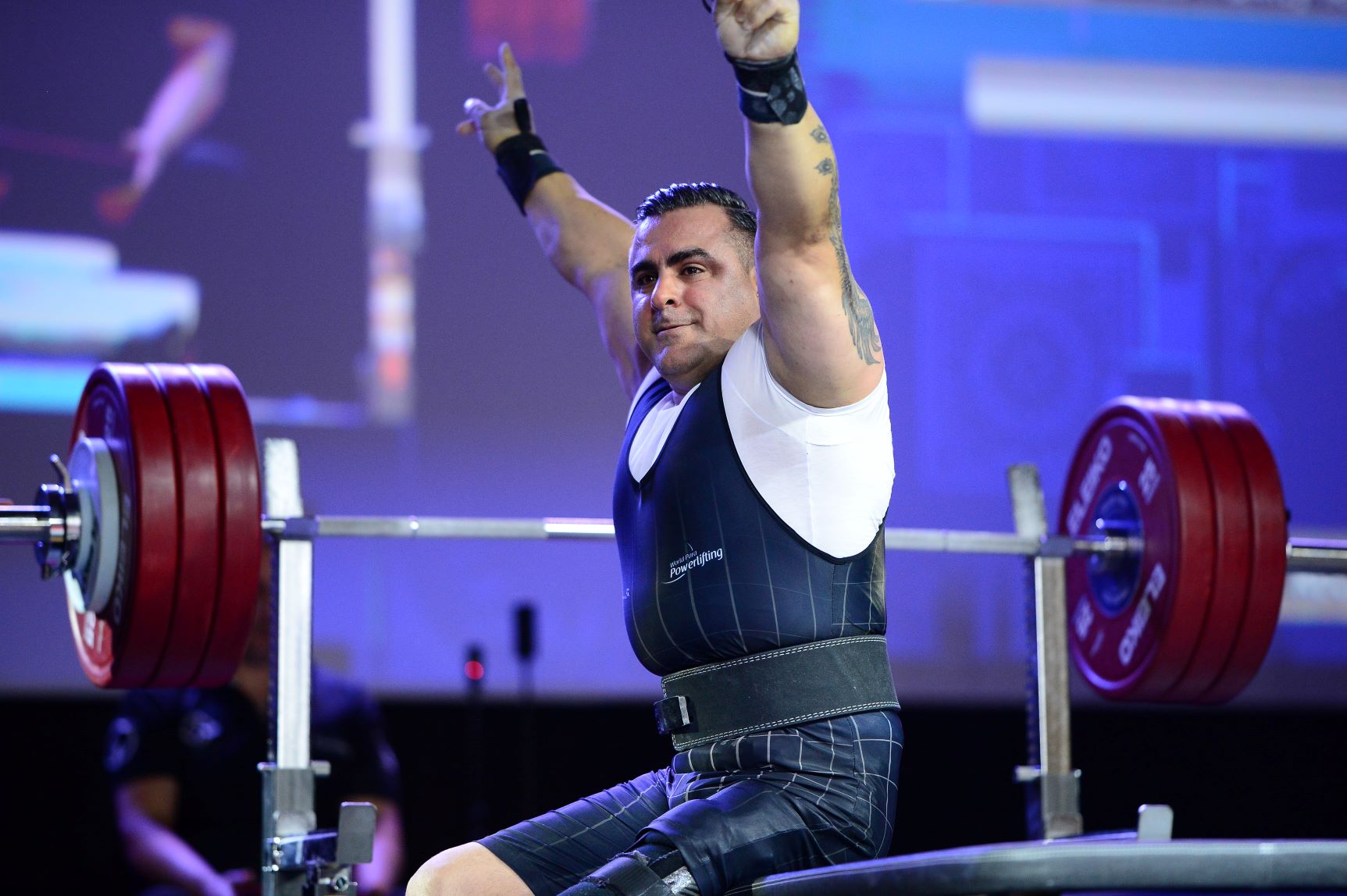 Para powerlifting athlete Hadi Darvishpoor sits in front of the weight and raises both arms.