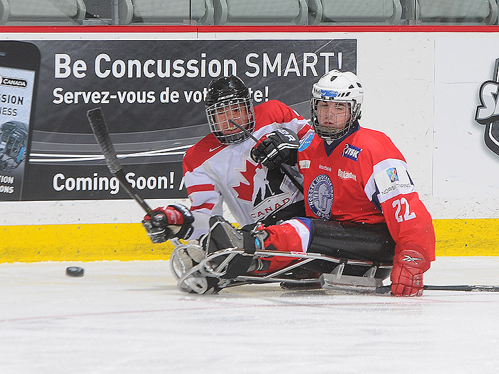 A picture of a two men in sledges playing ice hockey