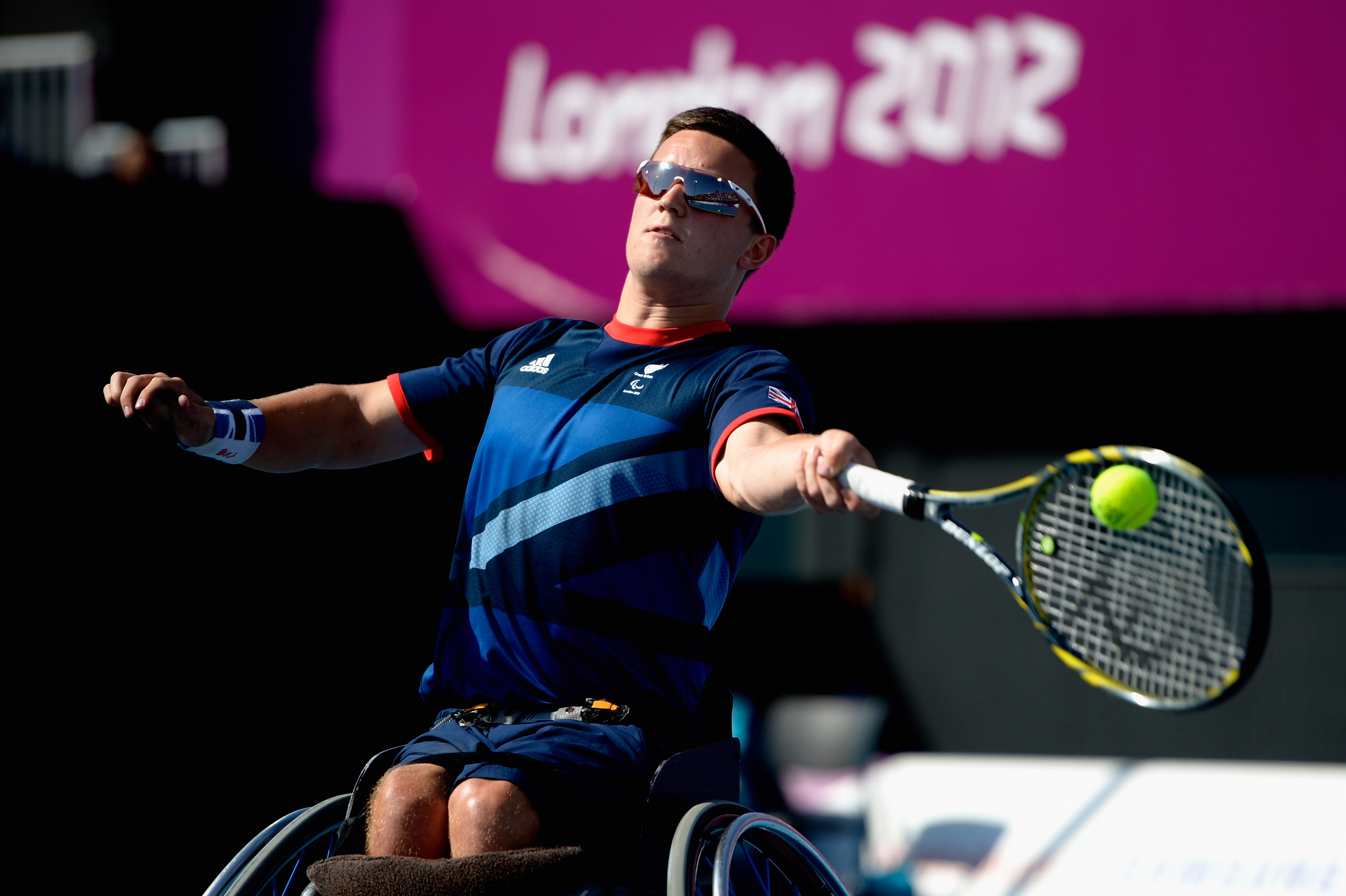 A picture of a man in a wheelchair playing a forehand during a wheelchair tennis game