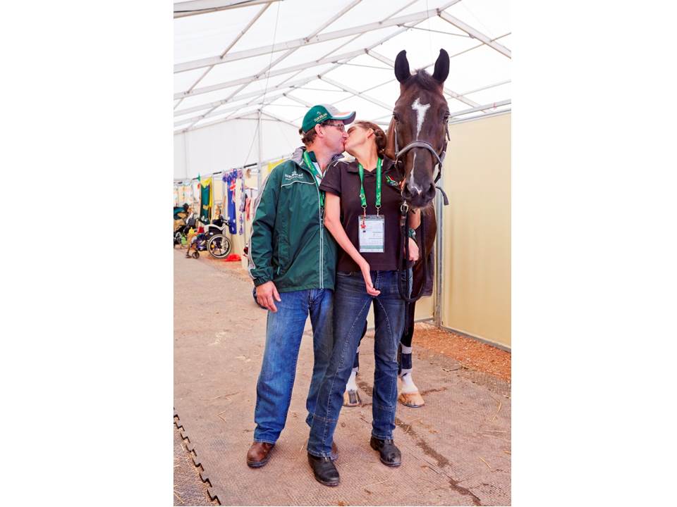 Man and women kissing, a black horse stands next to them.