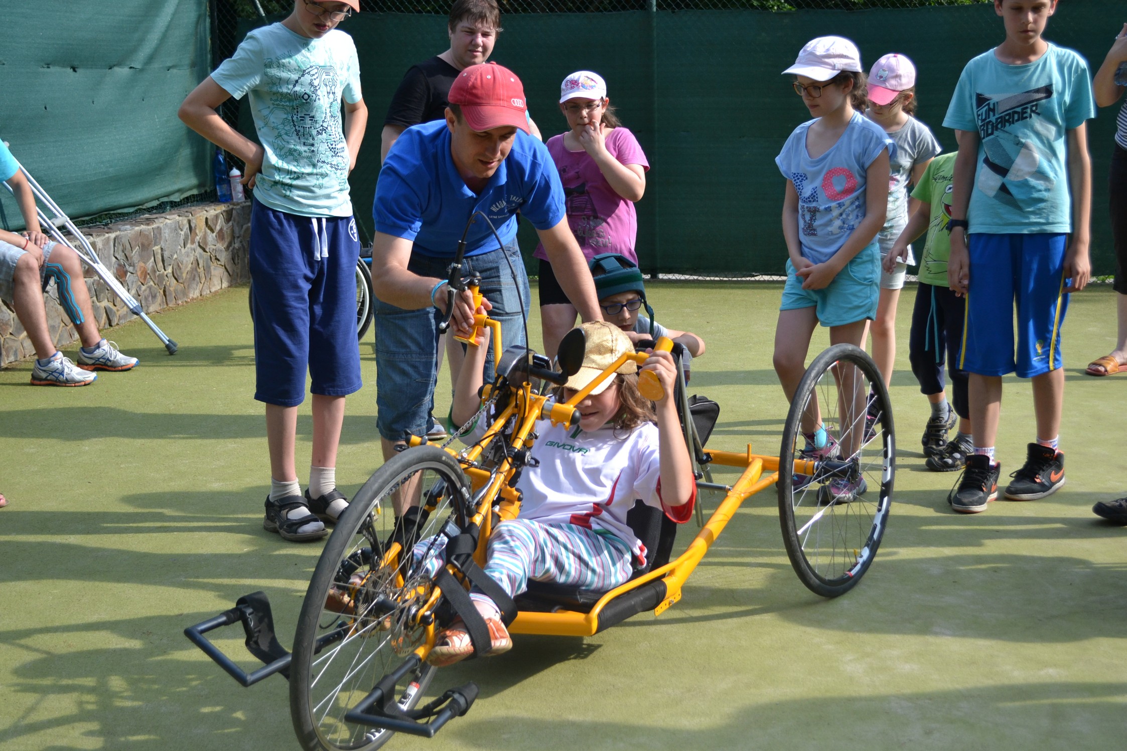 Kid in a handbike with other people standing around and watching