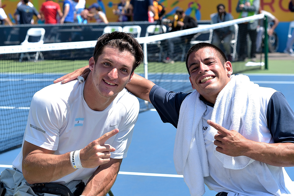 two tennis players smiling to the camera and pointing their index finger making a number 1 sign
