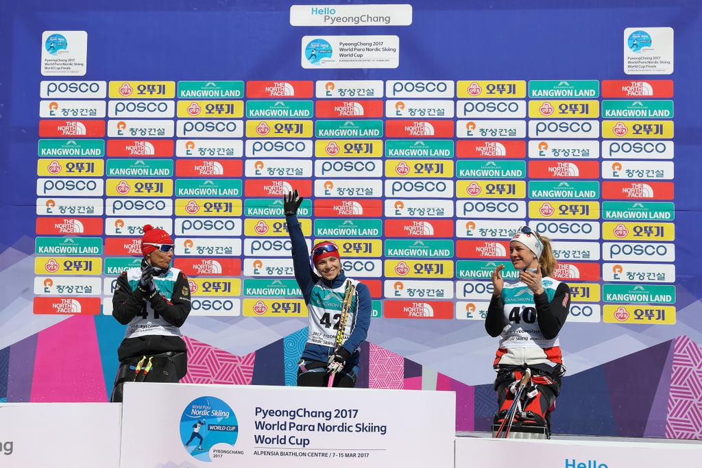 A sit skier raises her arm in the air to celebrate her victory