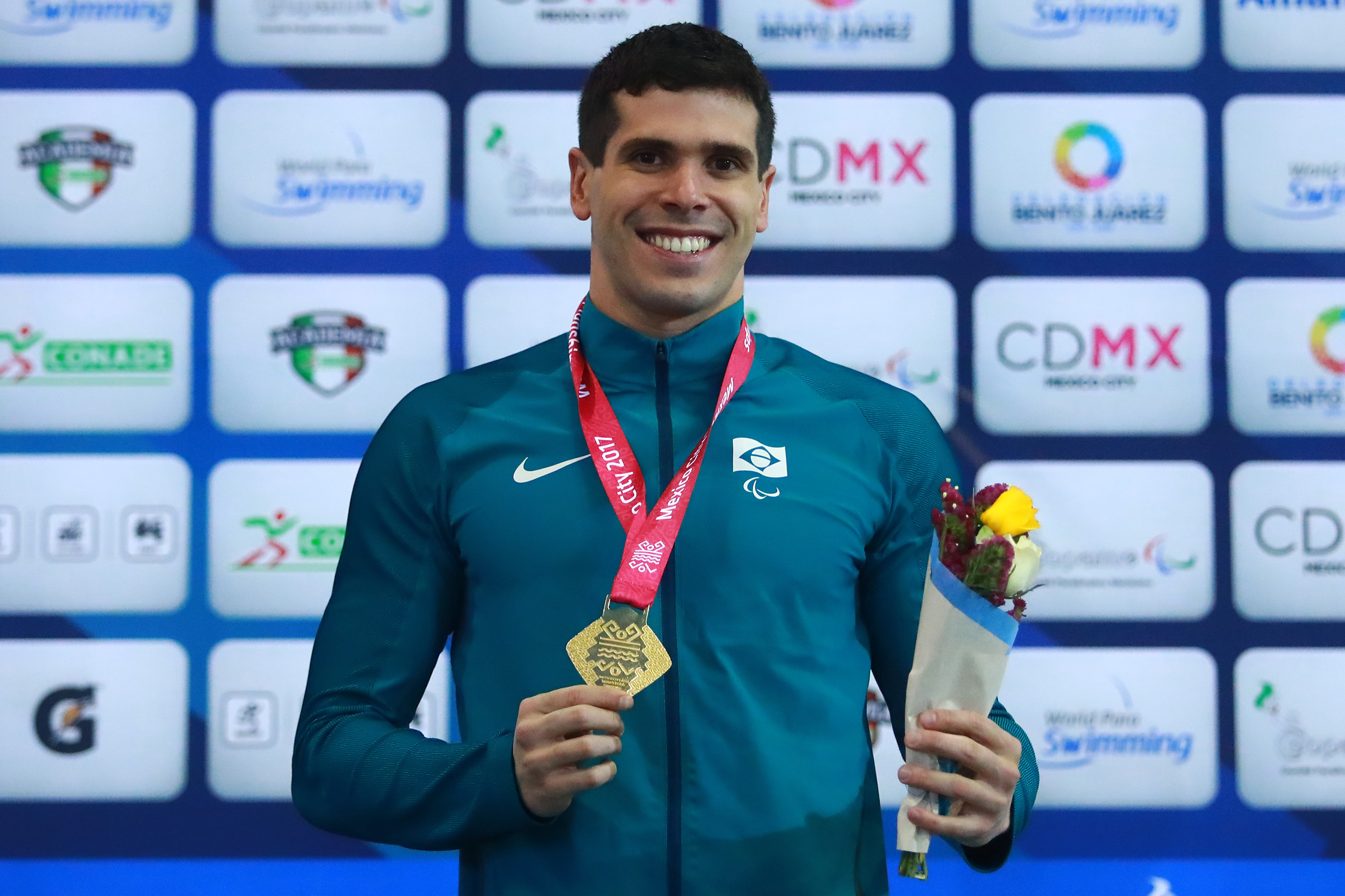 A male Para swimmer smiles holding his gold medal