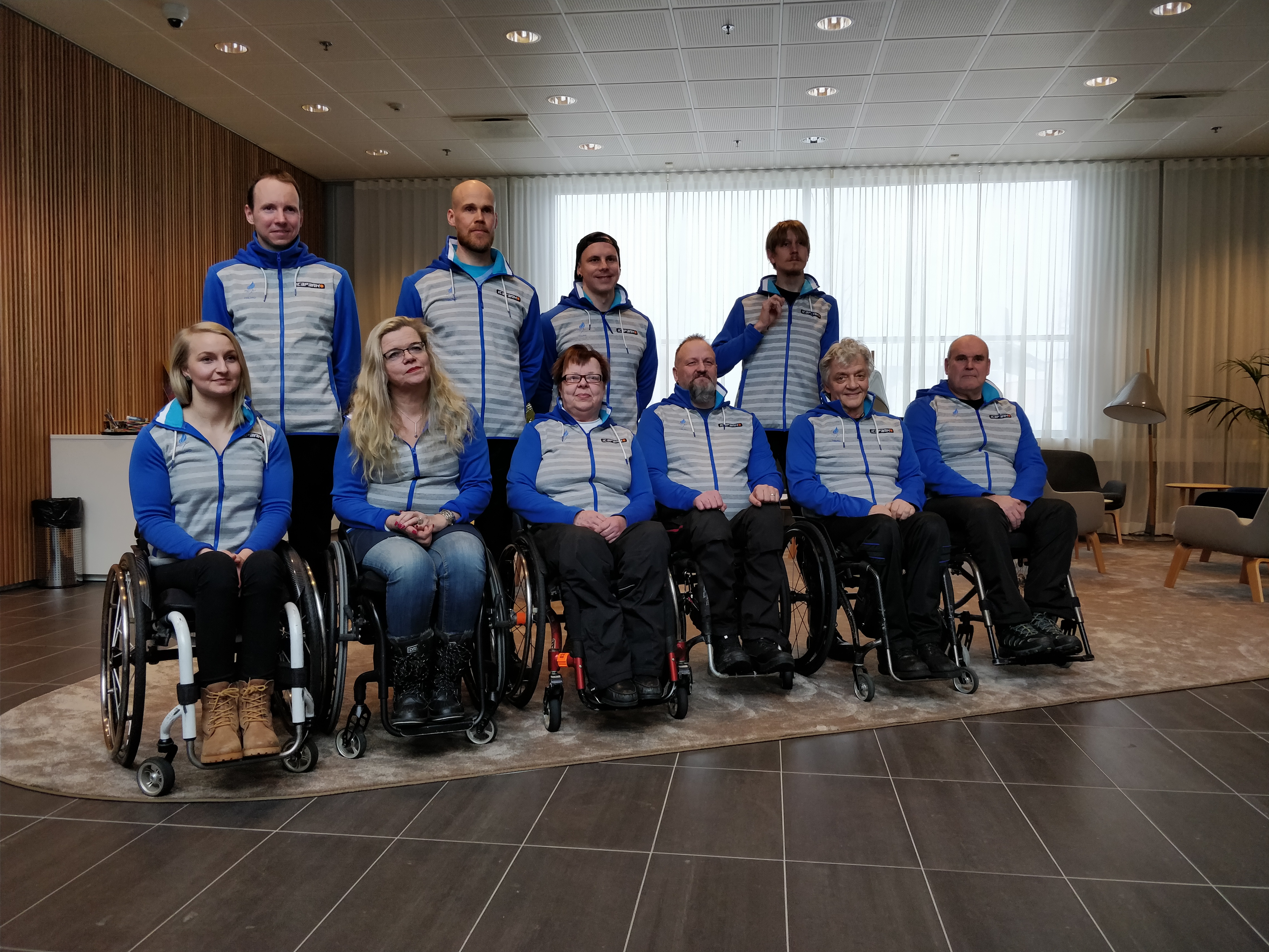 Four people standing behind a group of six people in wheelchairs