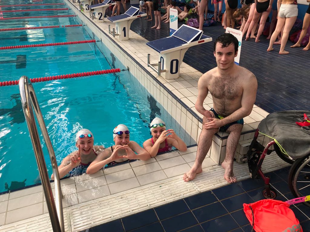 Three swimmers in the pool and one swimmer out of the pool posing for a picture