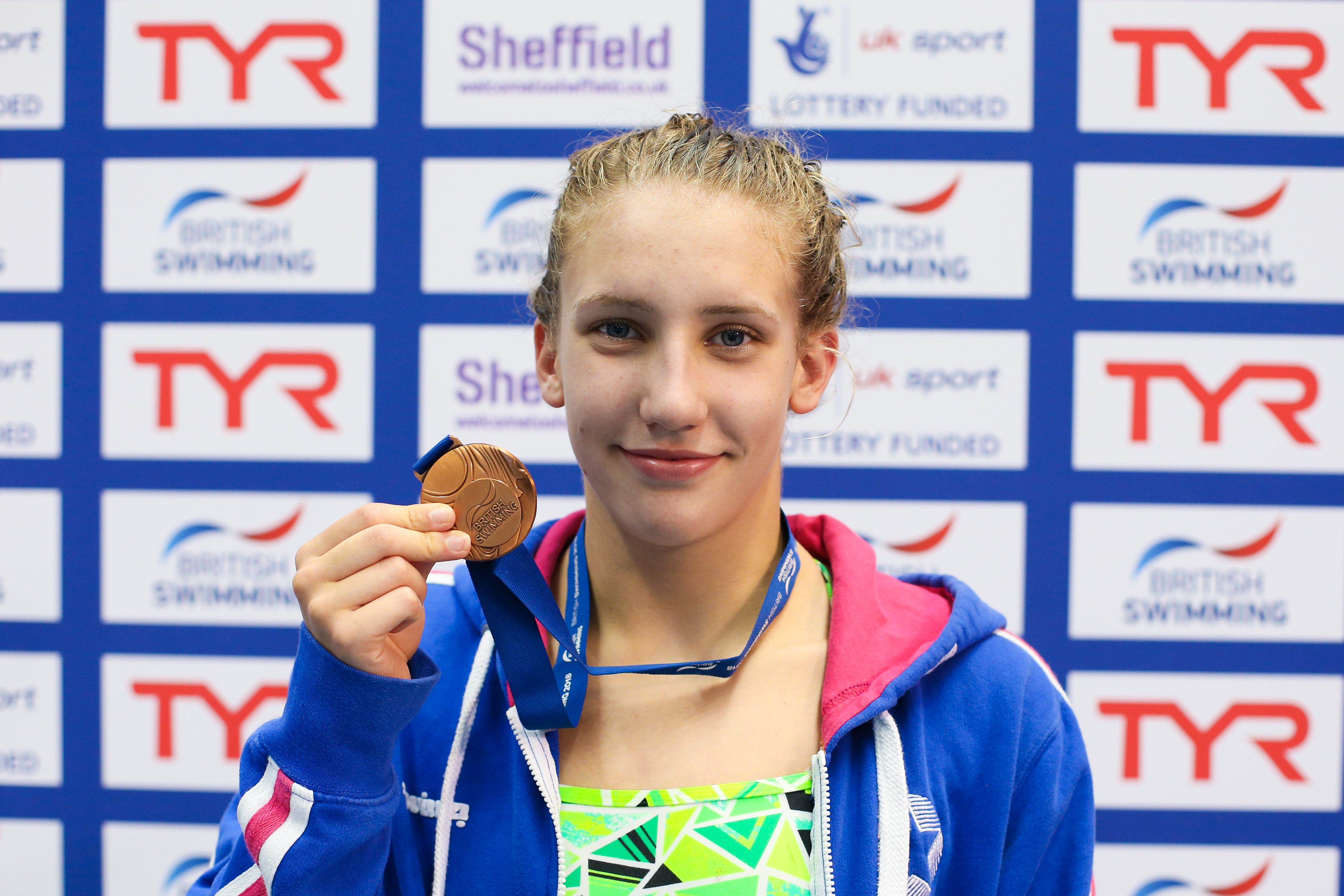 a female Para swimmer holds up a medal and smiles