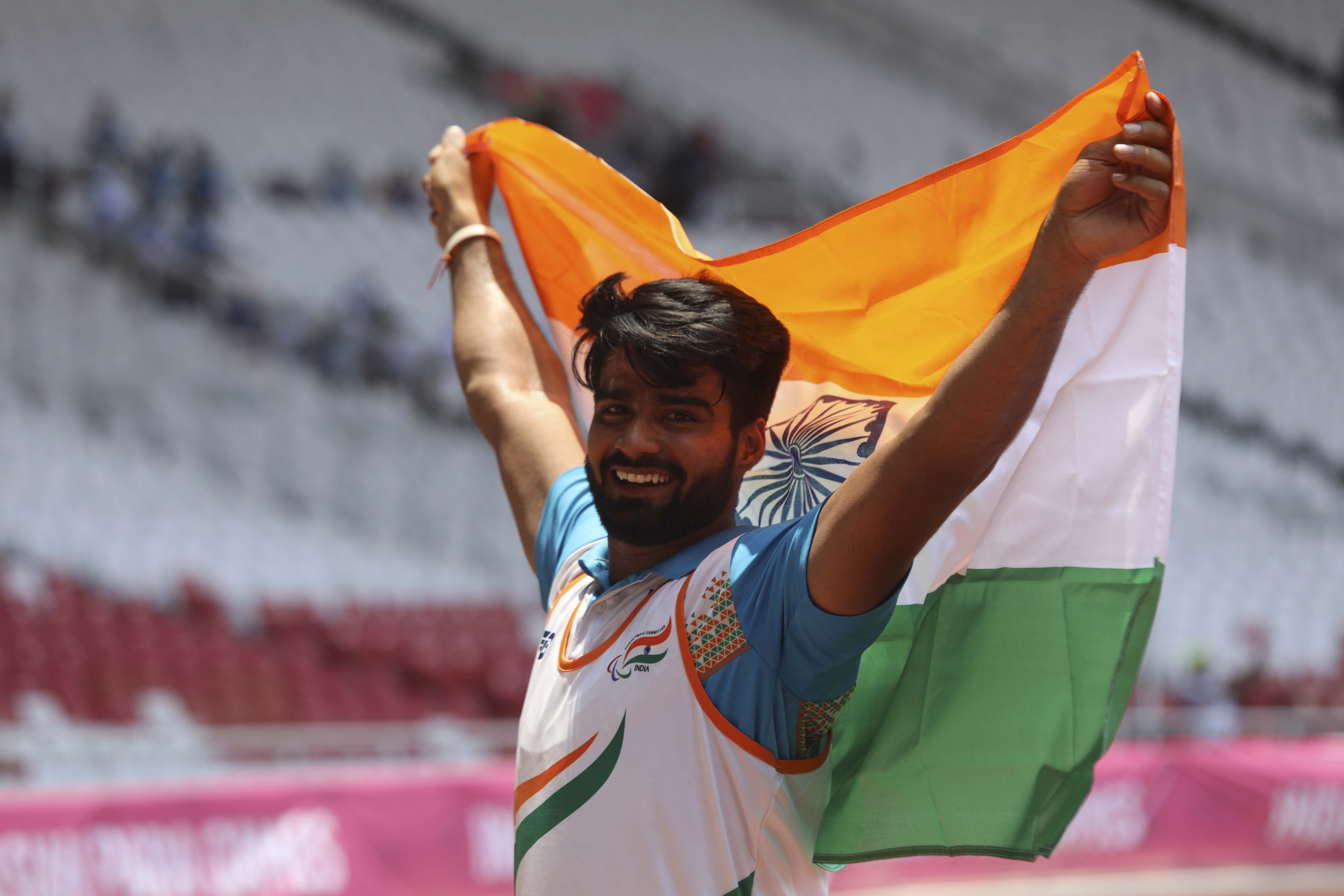 male Para athlete Sandeep Sandeep smiling and holding up an India flag