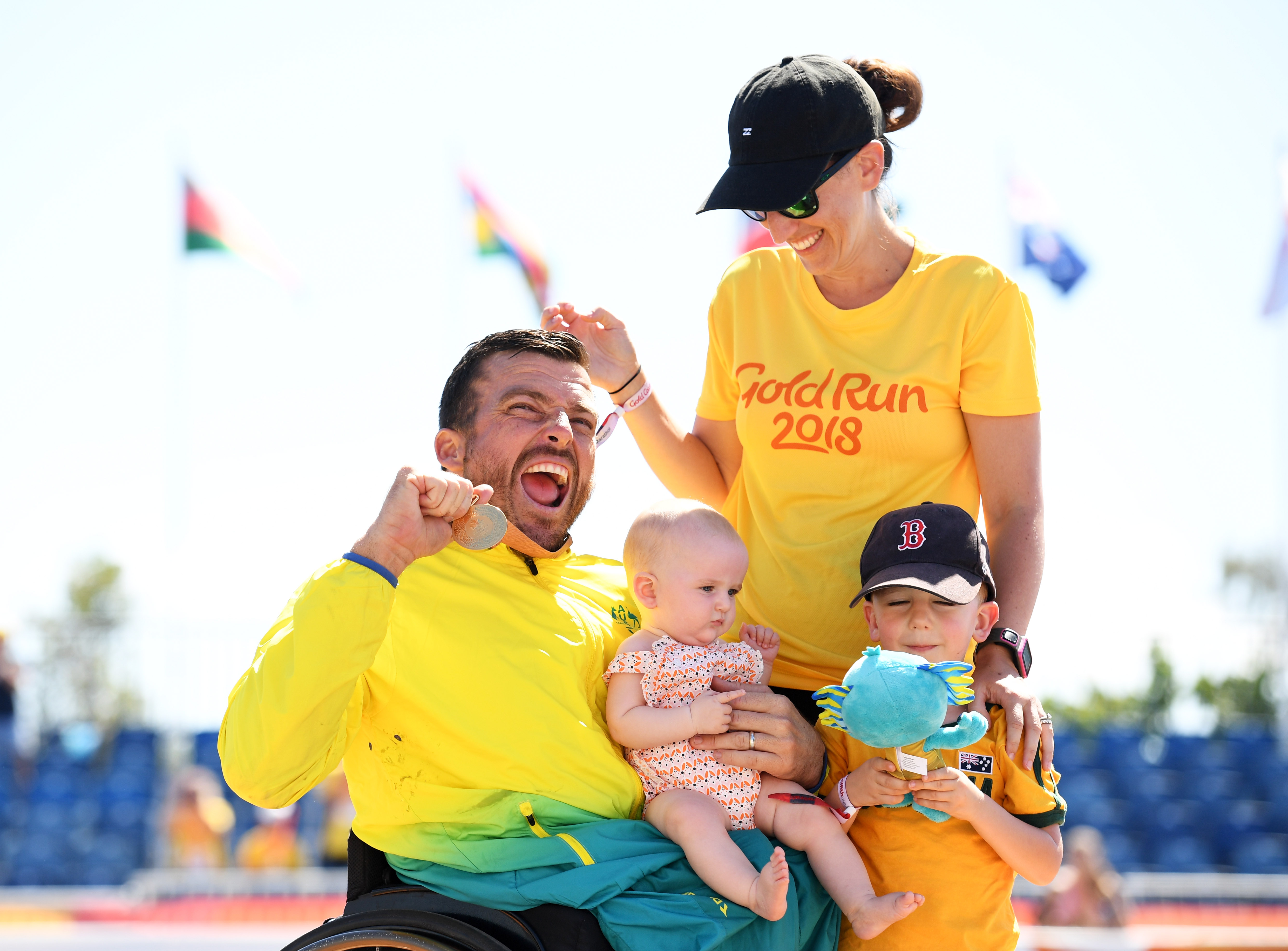 male wheelchair racer Kurt Fearnley holds up his medal alongside his wife and holding his child on his lap
