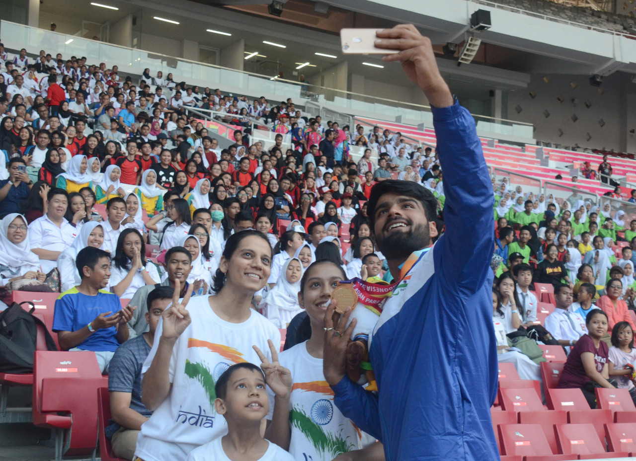 Man with a medal taking pictures with fans on the stands in a stadium