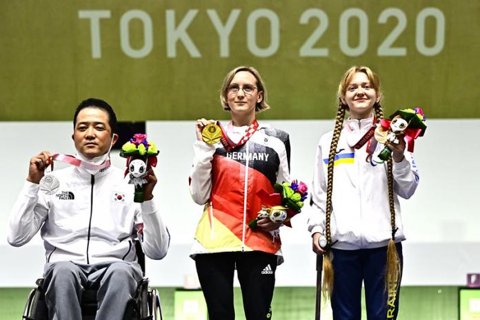 A man in a wheelchair standing next to two women on a podium