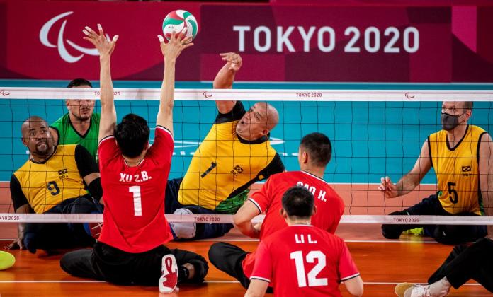 A male sitting volleyball athlete smashes a ball while a player in the opposing team blocks it