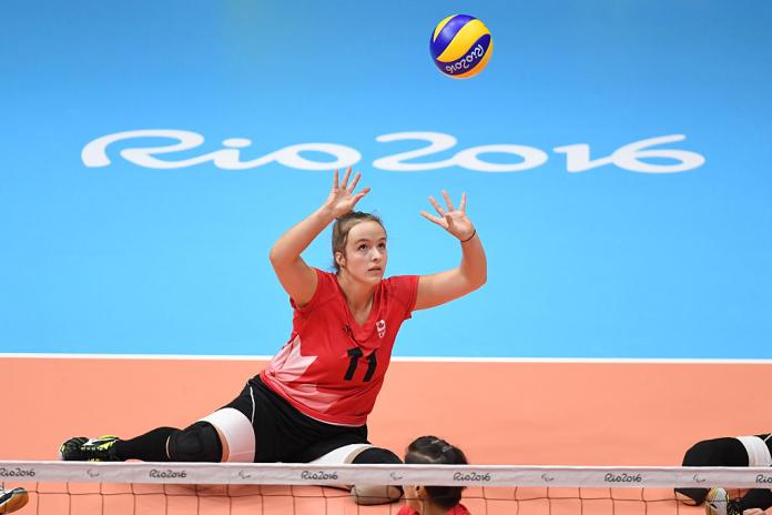 A female sitting volleyball athlete sets the ball during competition