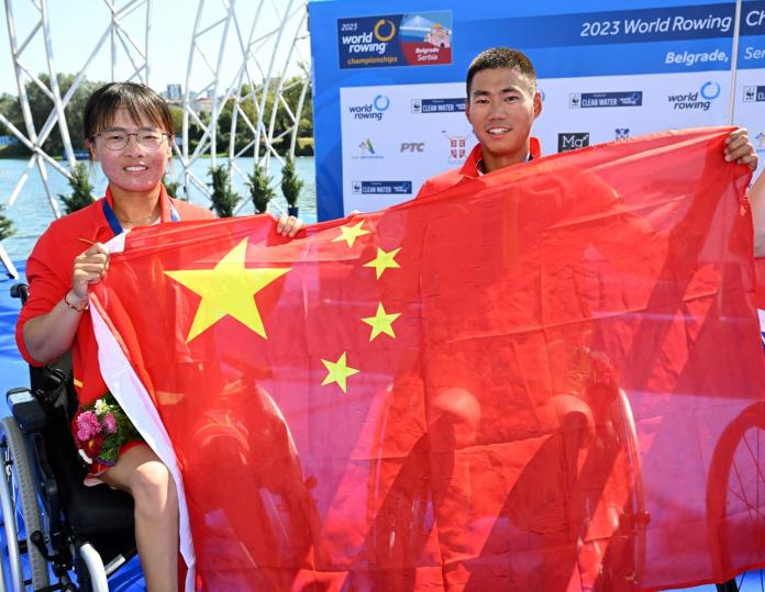 Two athletes pose for a photo while holding the flag of China