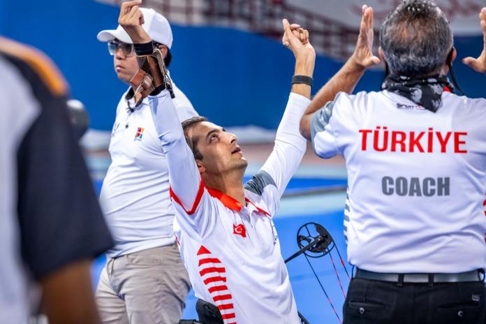 A male Para athlete reacts during competition by raising both hands