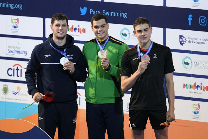 Three male athletes pose for a photo on the podium.