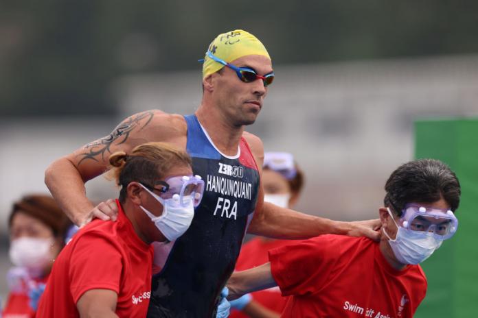 A male triathlete is assisted by staff after the swim segment at the Tokyo 2020 Paralympics