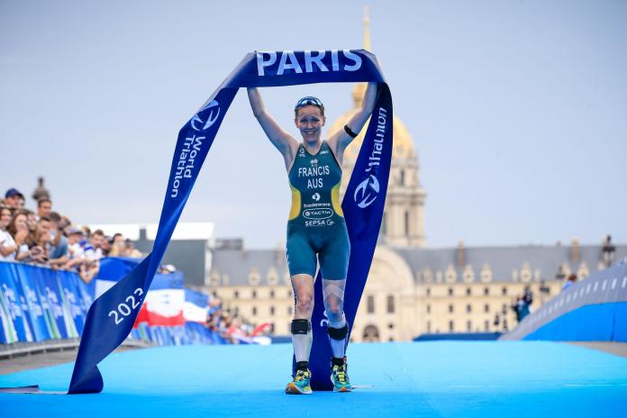 A female Para triathlete holds the finish tape that says Paris above her head