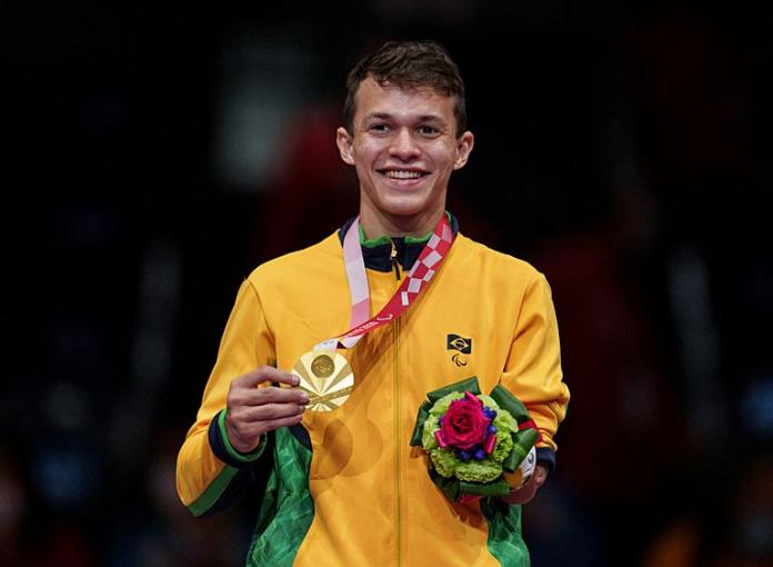 A male athlete wearing Brazil's yellow uniform poses for a photo after receiving a gold medal