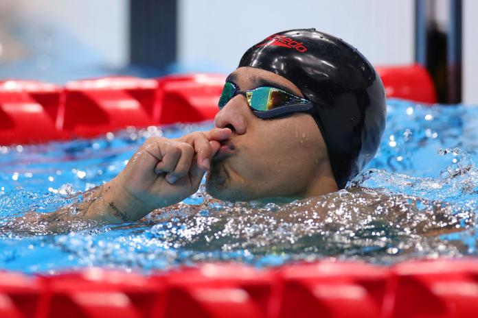 A male Para swimmer holds his hands to his lips in the pool after a competition
